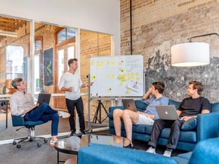 A team sitting in an office with an Executive Assistant talking about budgeting in front of a white board